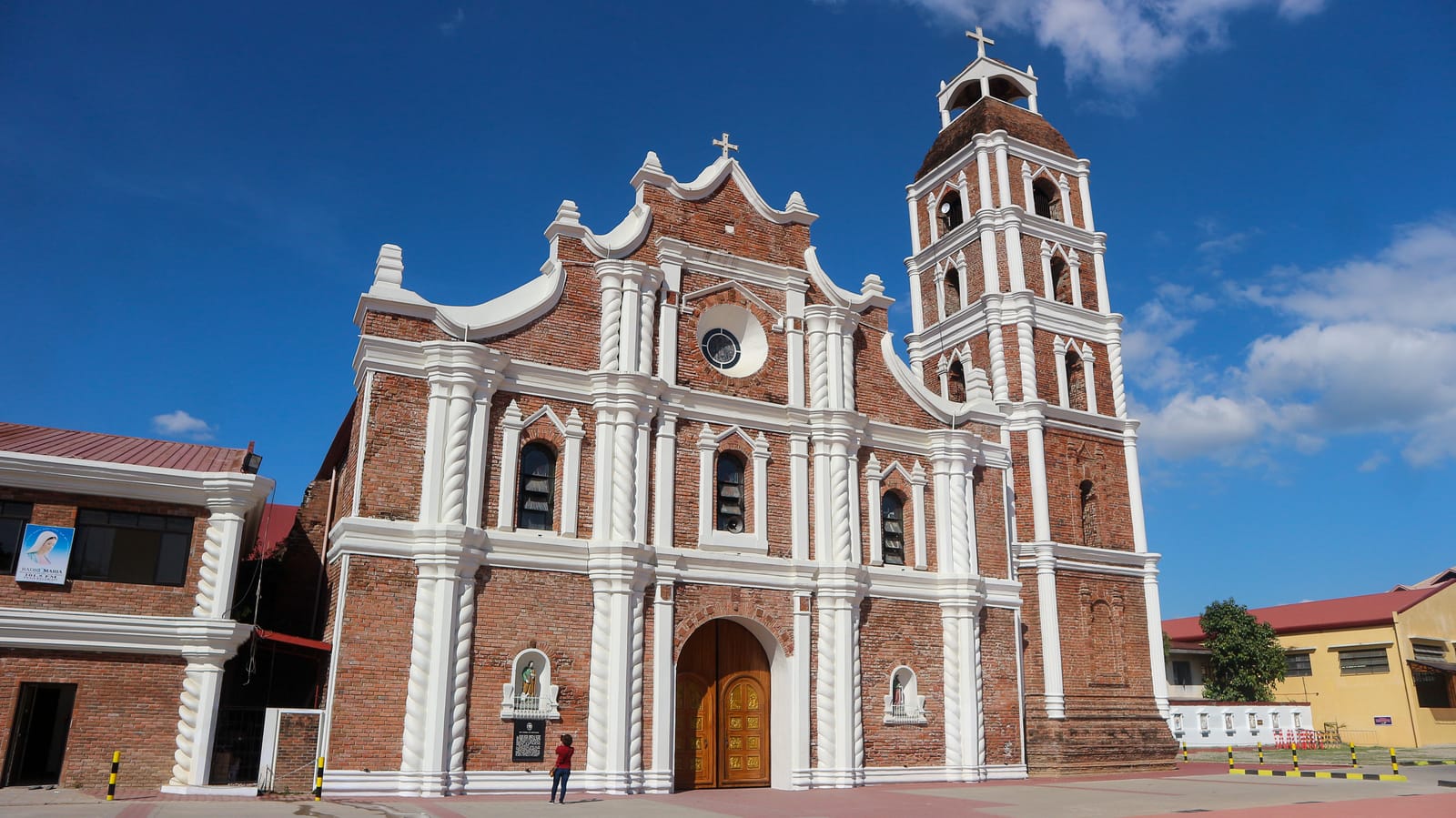 A red-brick church with a white-trimmed, scrolled facade and a tall bell tower topped by a cross, under a deep blue sky.