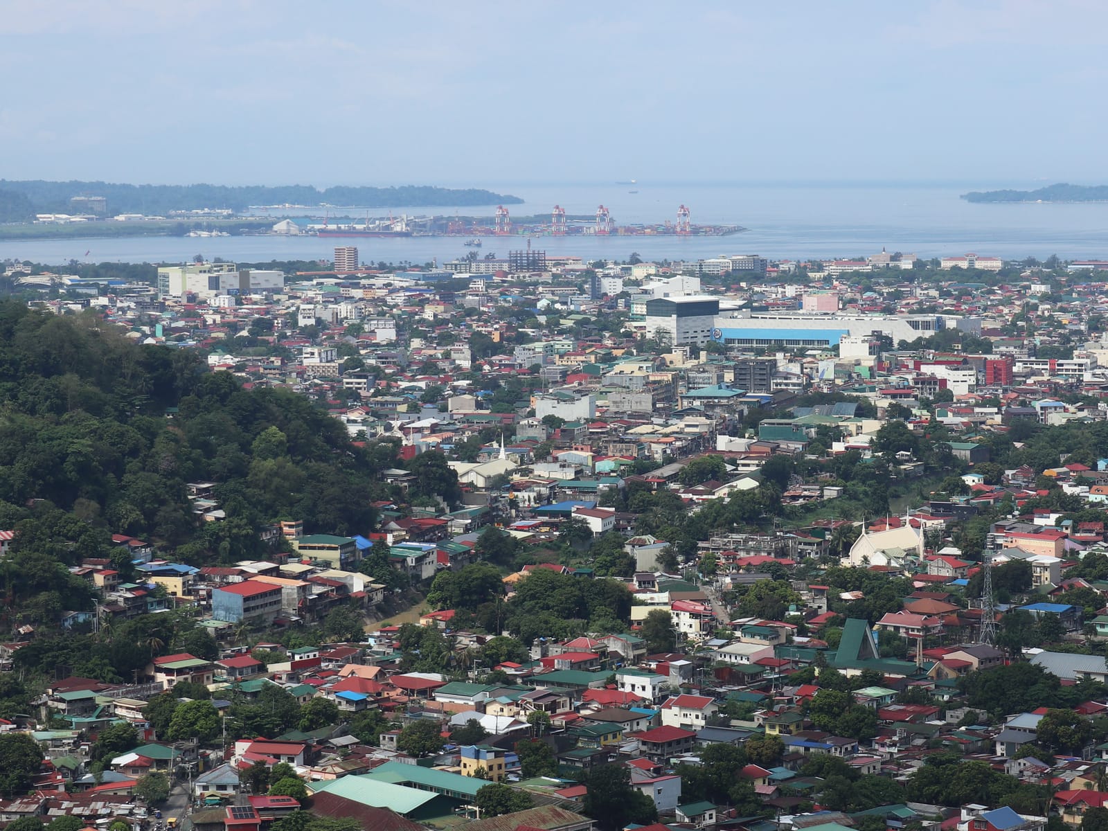 Rooftops of Olongapo City filling the plain below a green hill, with the port of the Subic Bay Freeport and the bay beyond.